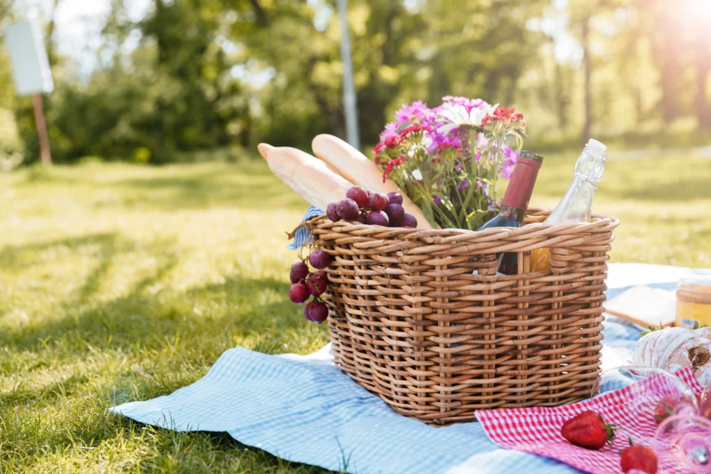 French picnic basket with baguettes, grapes, wine, and flowers on a summer lawn near Paris