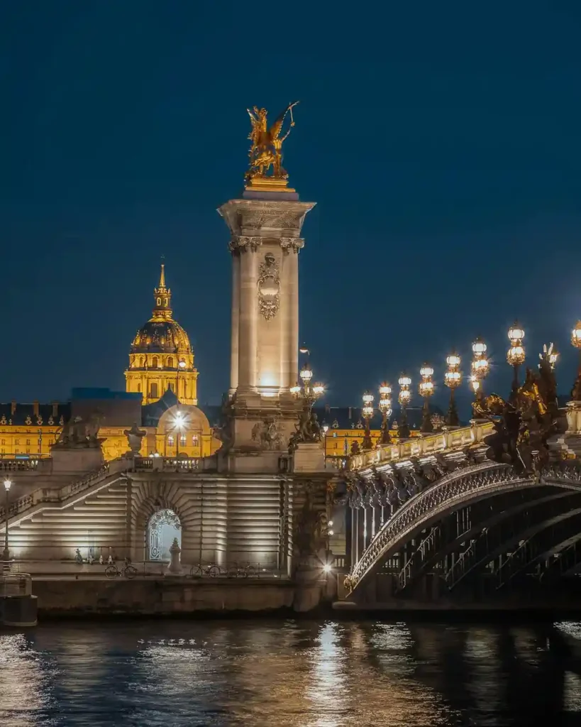 Pont Alexandre III in Paris illuminated at night with view of Les Invalides dome in background