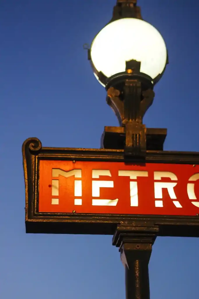 Classic red Paris Métro sign with art nouveau lamp against a clear blue sky