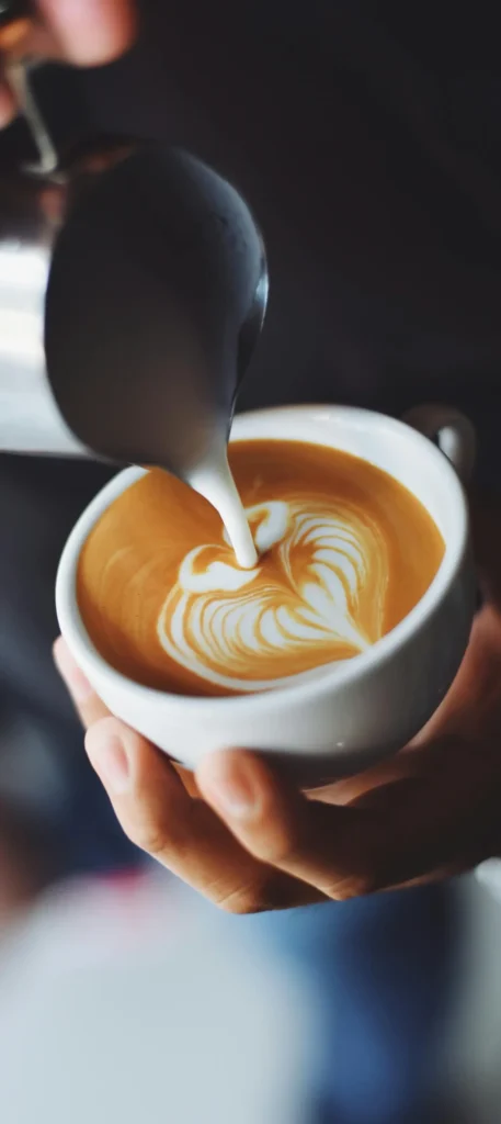 Barista pouring steamed milk into a cup of artisan coffee