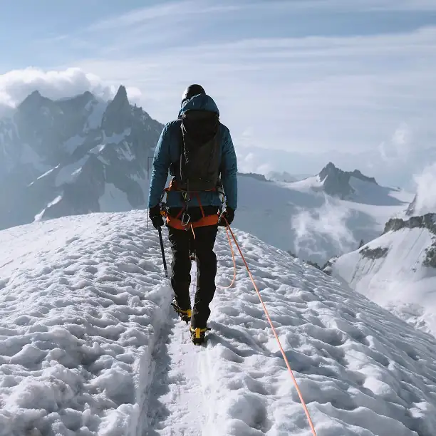 Hiker walking along a glacier ridge with alpine peaks in the background
