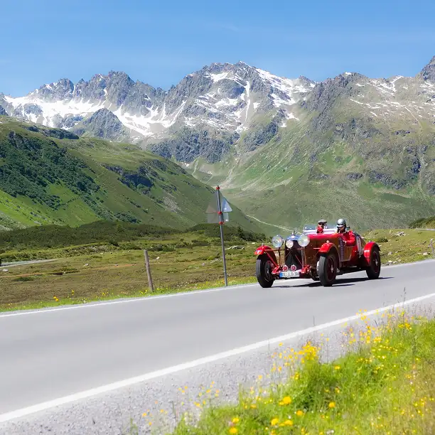 Vintage red car driving along a winding alpine road in the French mountains