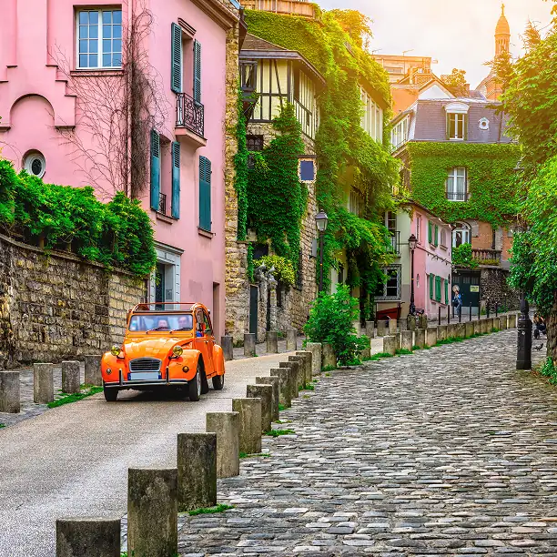 Classic car parked on a cobbled street near ivy-covered buildings in Montmartre