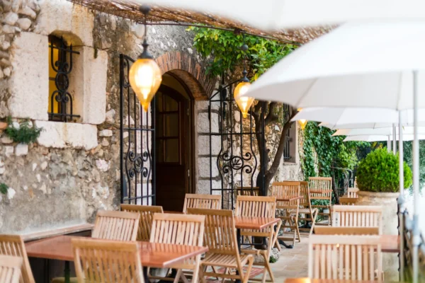 Outdoor dining area with stone walls, ironwork, wooden chairs, and umbrellas in a French restaurant