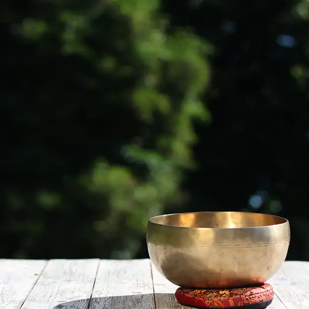 Golden Tibetan singing bowl placed on a wooden deck outdoors