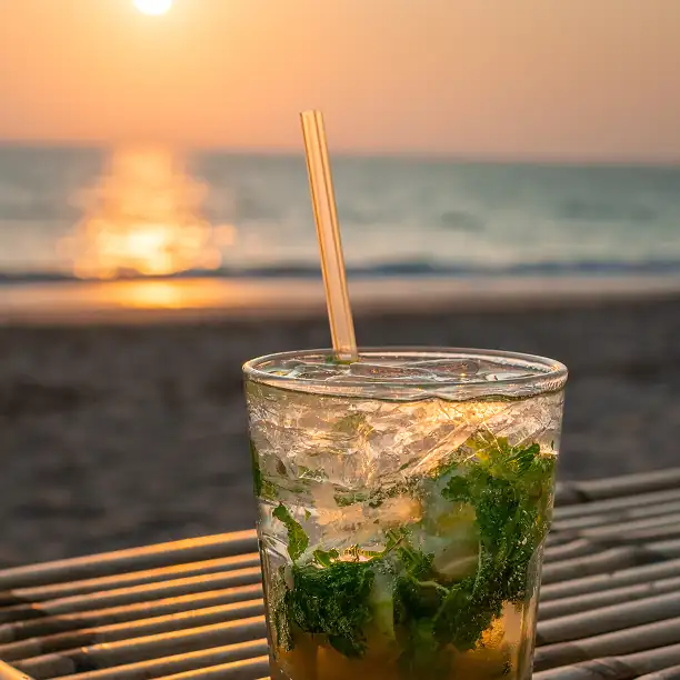 Cocktail glass at golden hour on a beachside table with ocean view