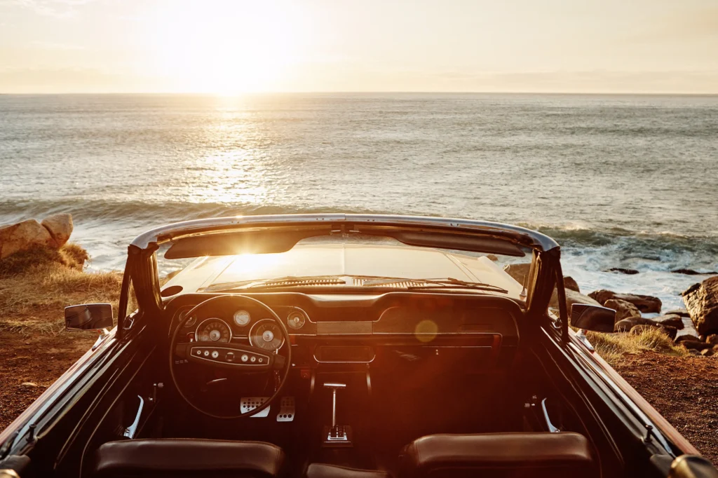 Couple driving a vintage convertible at sunset by the coast
