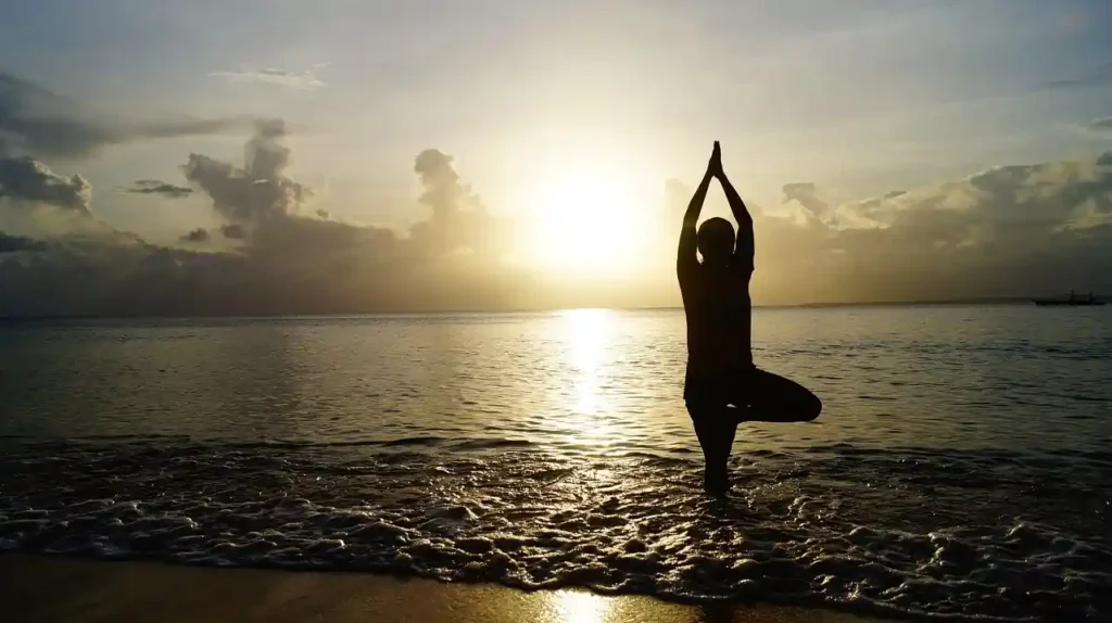 Woman practicing yoga by the ocean at sunrise