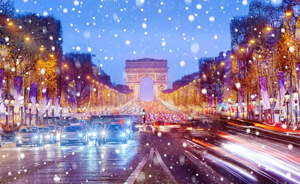 Snow falling around the Arc de Triomphe lit up with holiday lights