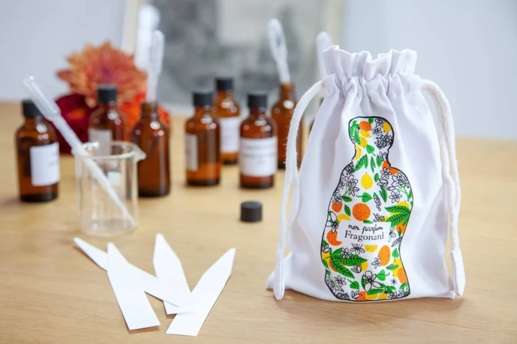 Menton, élégant pochon blanc avec flacons de parfum français de luxe et huiles essentielles disposés sur une surface naturelle