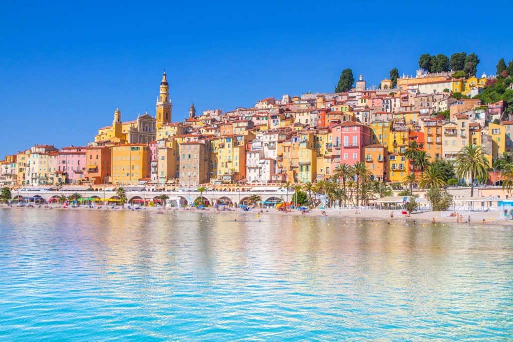 Picturesque Menton village with colorful pastel buildings, historic bell tower, and Mediterranean beach on French Riviera