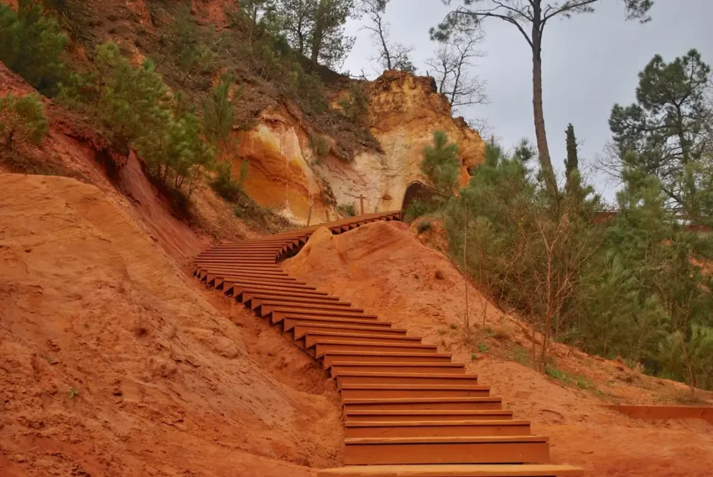 Wooden staircase winding through dramatic red ochre cliffs in Roussillon Provence under blue sky
