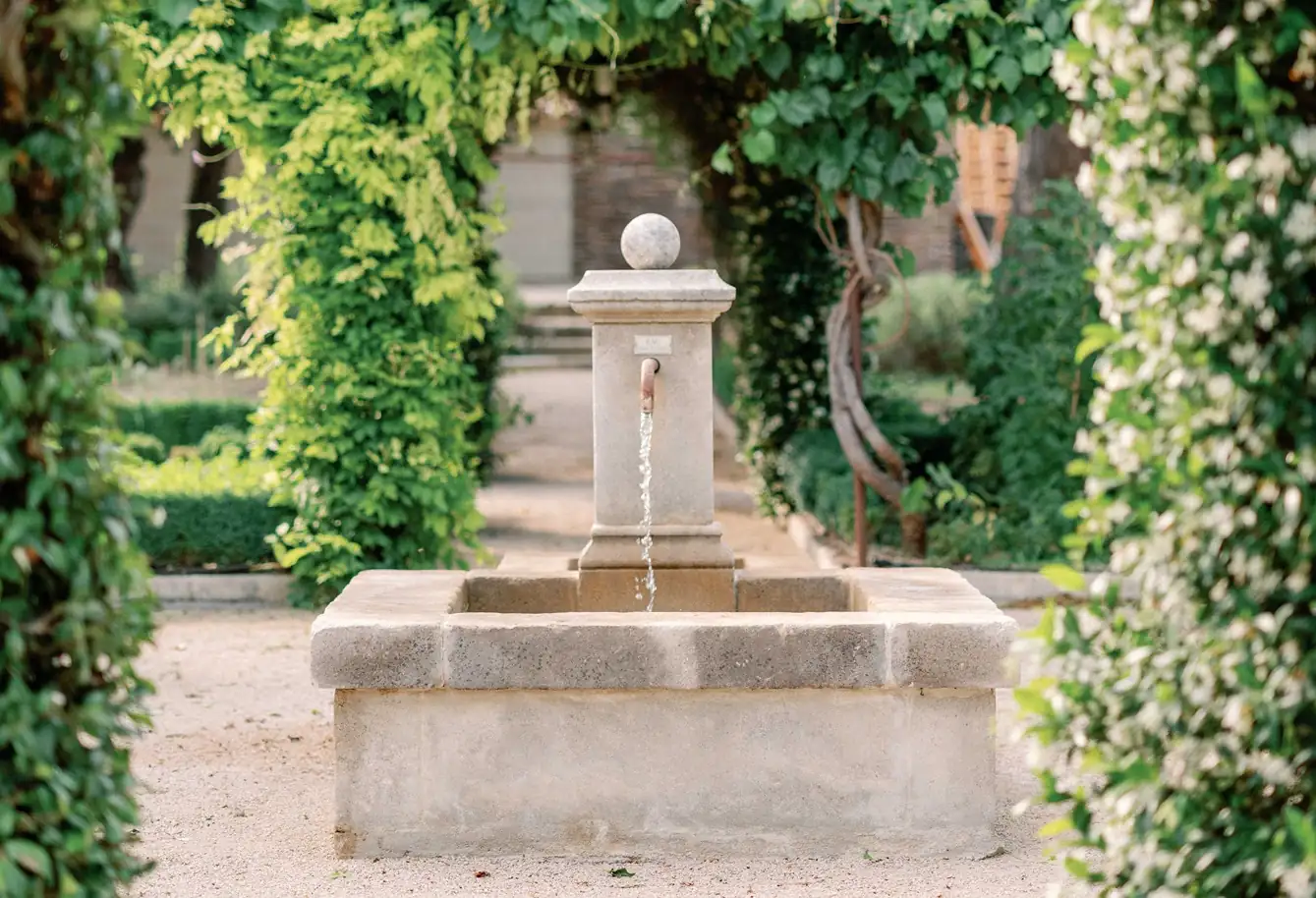 Traditional stone water fountain flowing in a lush, green Provençal courtyard garden