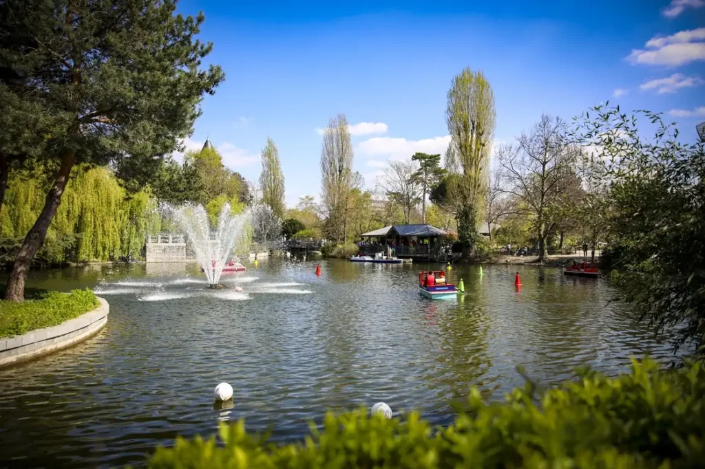 Lake with fountains, boats and lush trees at a family park in Paris.