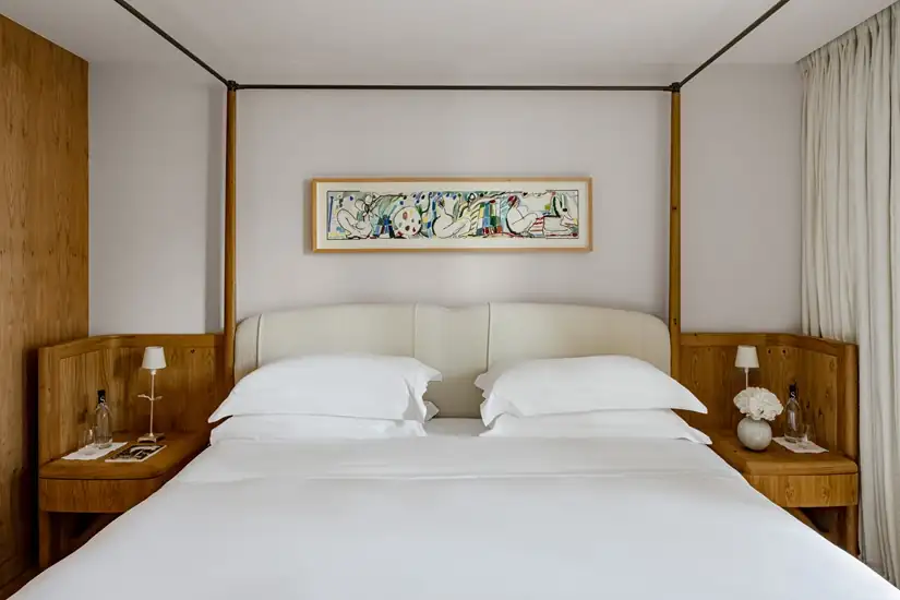 Elegant boutique hotel bedroom with white linens, botanical artwork, and warm wood accents in Paris