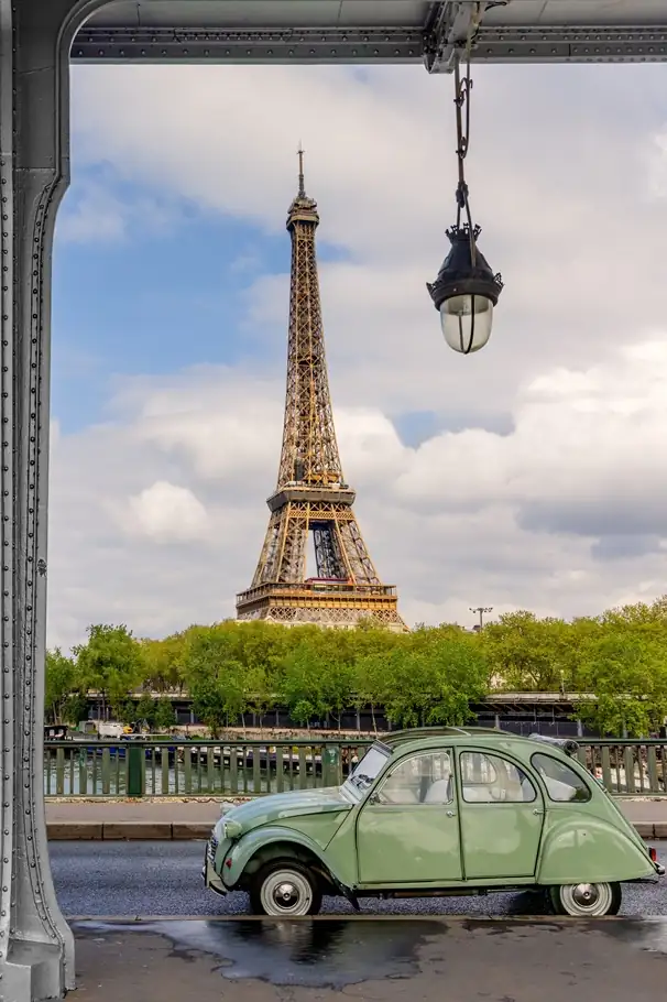 Eiffel Tower view from a Paris balcony with string lights and a vintage car parked below.