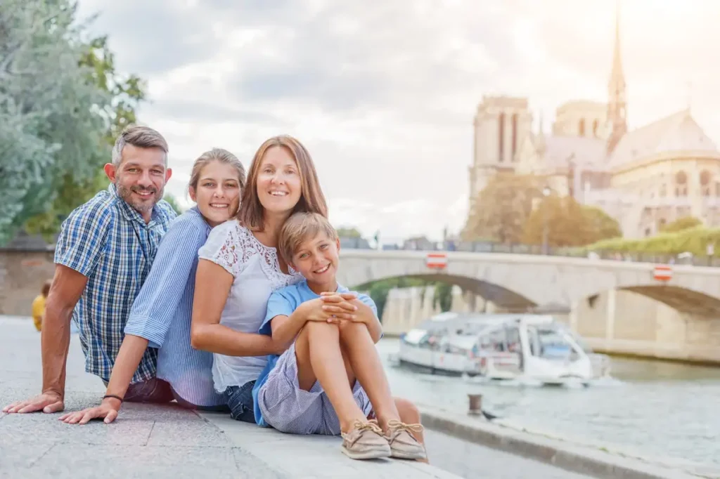 Smiling family with child relaxing on the Seine riverbank in Paris with Notre Dame in the background.