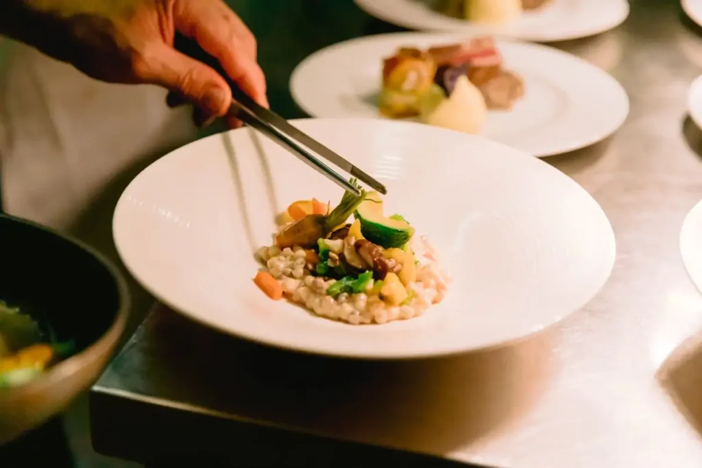 Private chef meticulously plating a gourmet dish with tweezers in a luxury kitchen