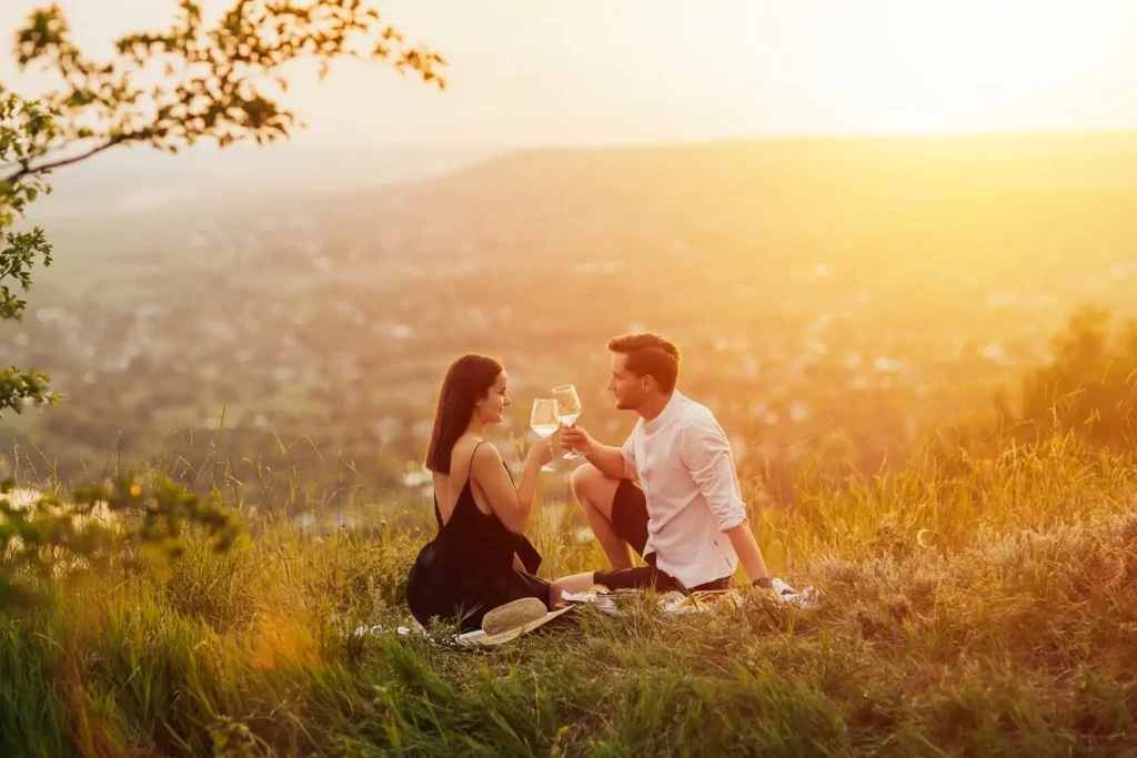 Couple enjoying a glass of white wine during a romantic sunset picnic overlooking a valley