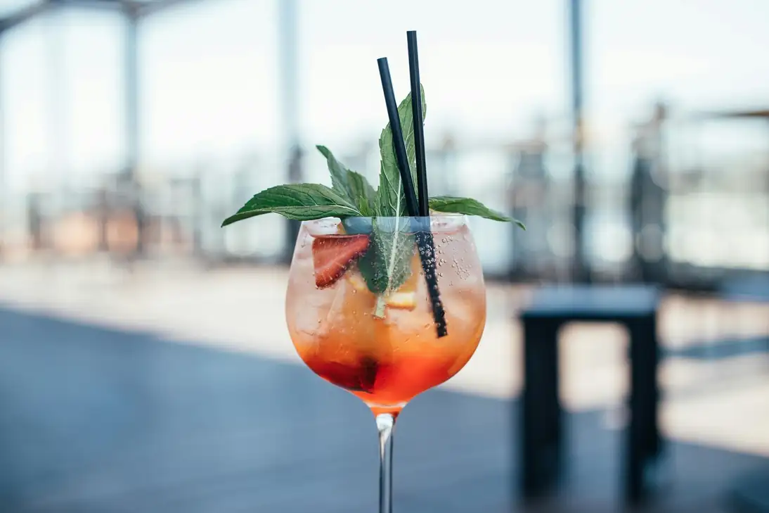 Refreshing orange spritz cocktail with basil garnish on a terrace with a blurred sunset background