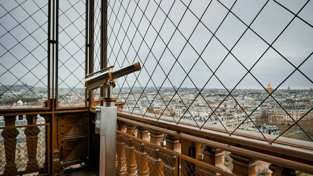 Telescope on the Eiffel Tower observation deck overlooking Paris rooftops