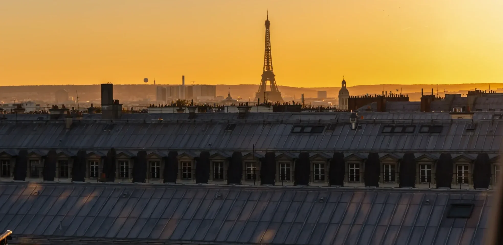 Golden-hour view of the Eiffel Tower rising above classic Paris rooftops