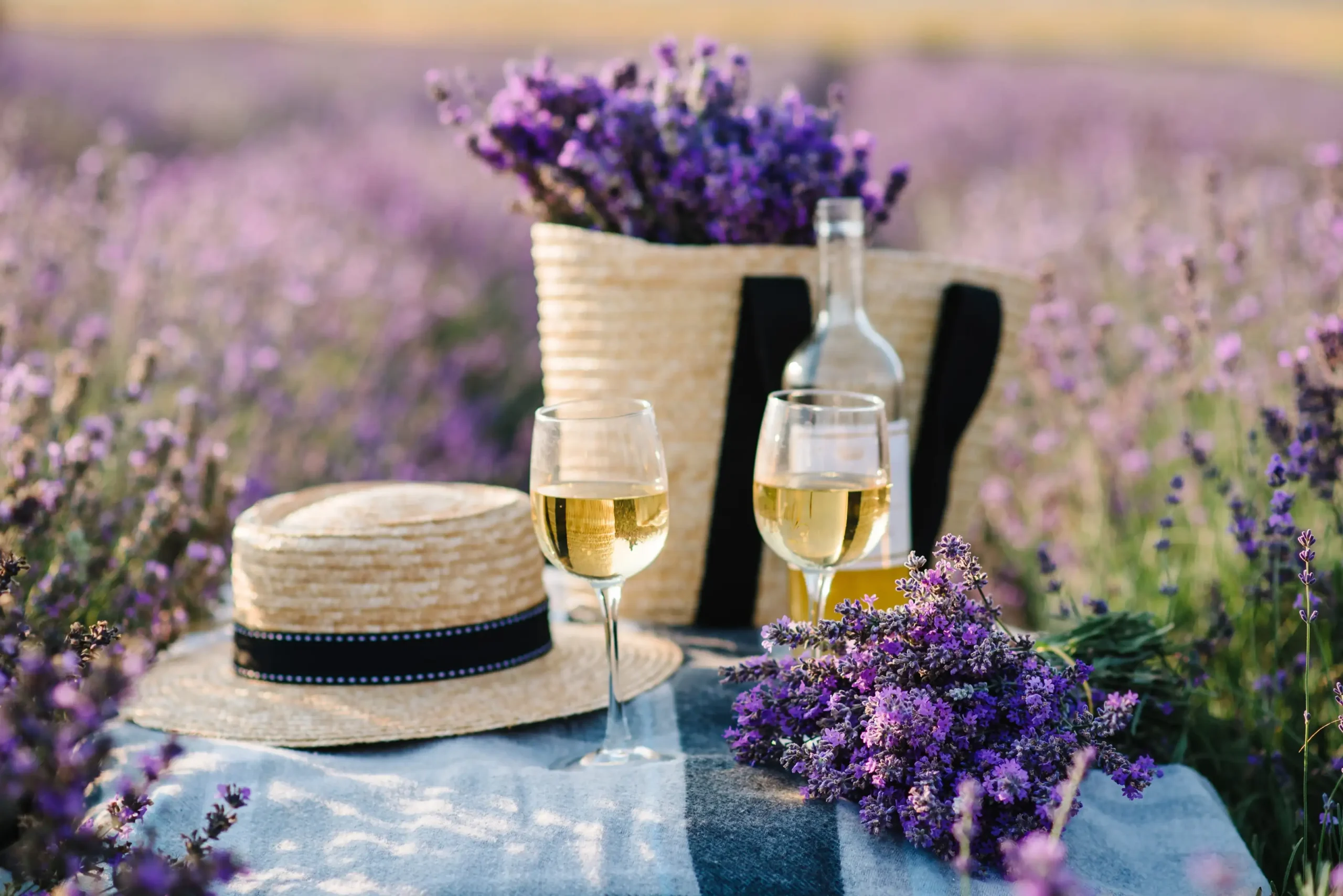 Romantic picnic setup with white wine and a straw hat in a blooming lavender field