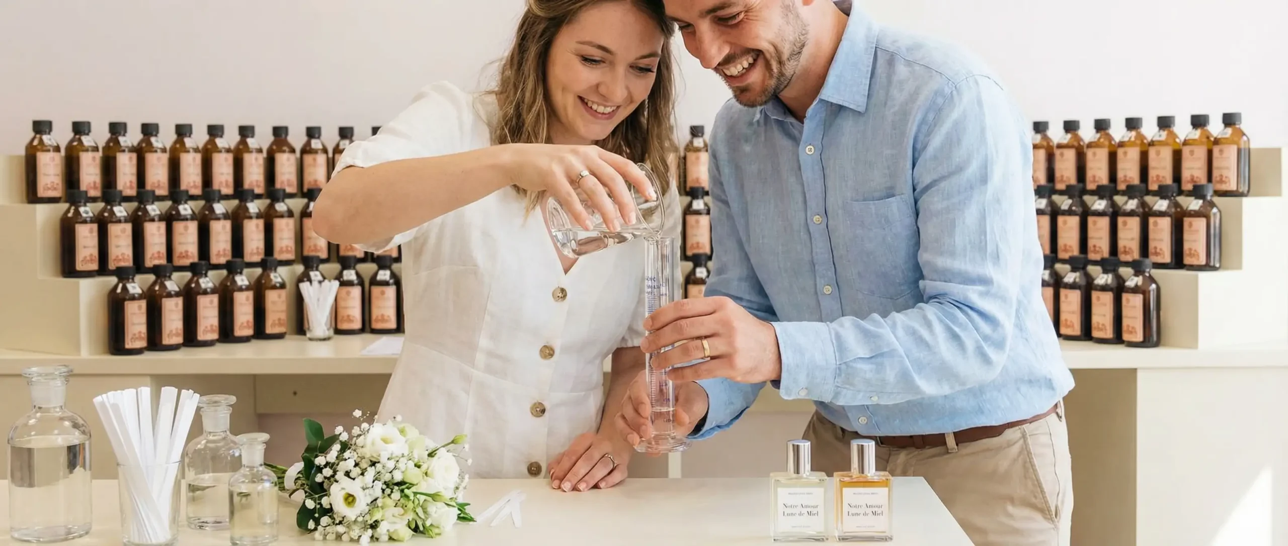 A smiling couple pouring essential oils into a graduated cylinder during a custom perfume making workshop.