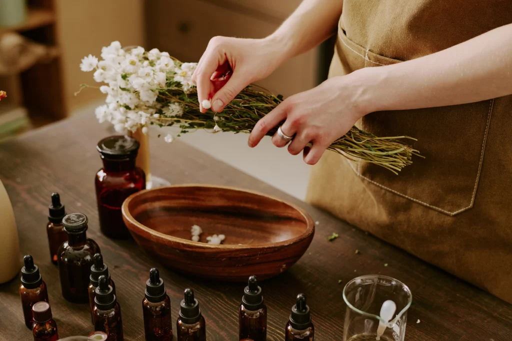 wellness travel France, Hands of an apothecary arranging dried white flowers near essential oil bottles