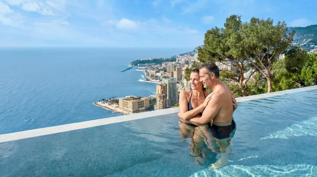 A couple relaxing in a cliffside infinity pool overlooking the Mediterranean coast and Monaco.