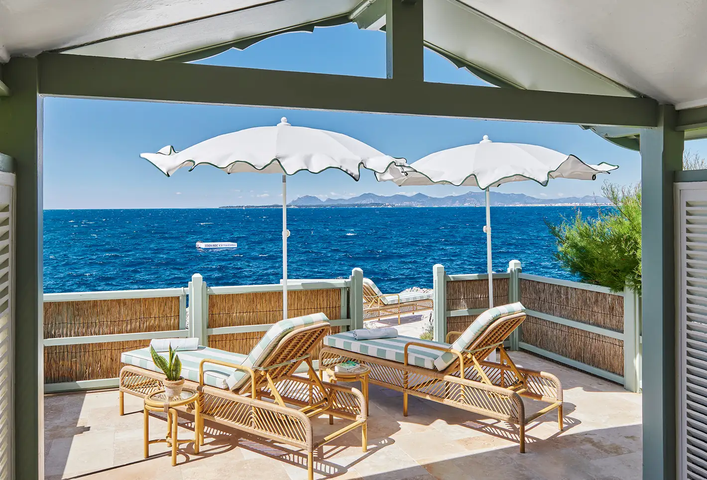 Elegant white parasols and wooden lounge chairs on a private terrace overlooking the sea.
