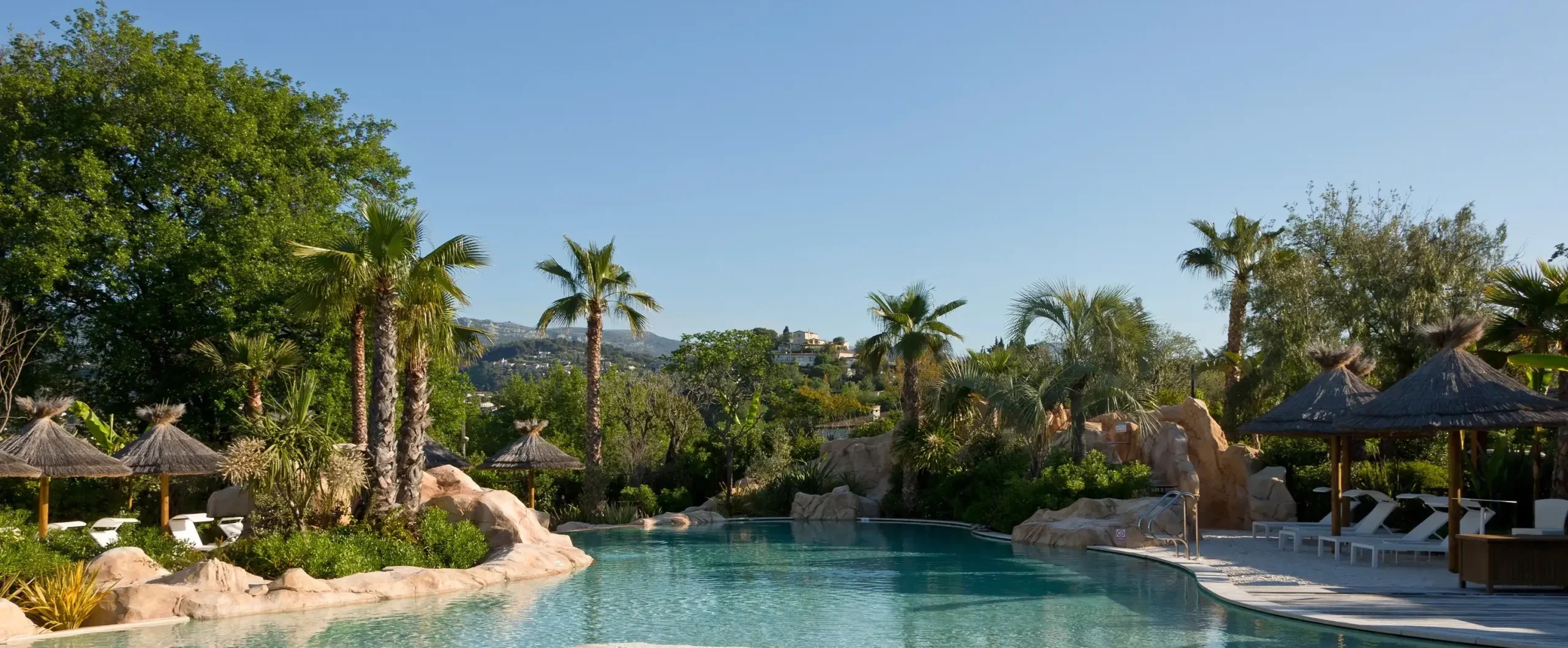 Crystal clear lagoon-style pool with white sand and palm trees at a Mediterranean resort