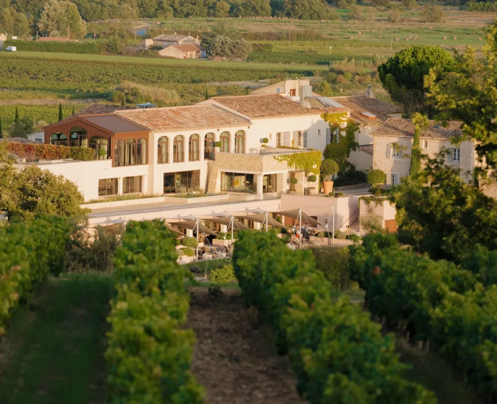 Aerial view of a luxury stone villa and winery surrounded by rows of green vineyards at sunset.
