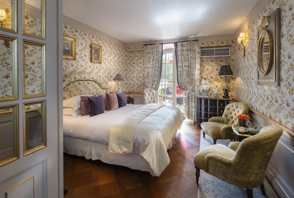 Interior view of an elegant bedroom suite featuring vintage patterned wallpaper, a plush king bed, and antique decor