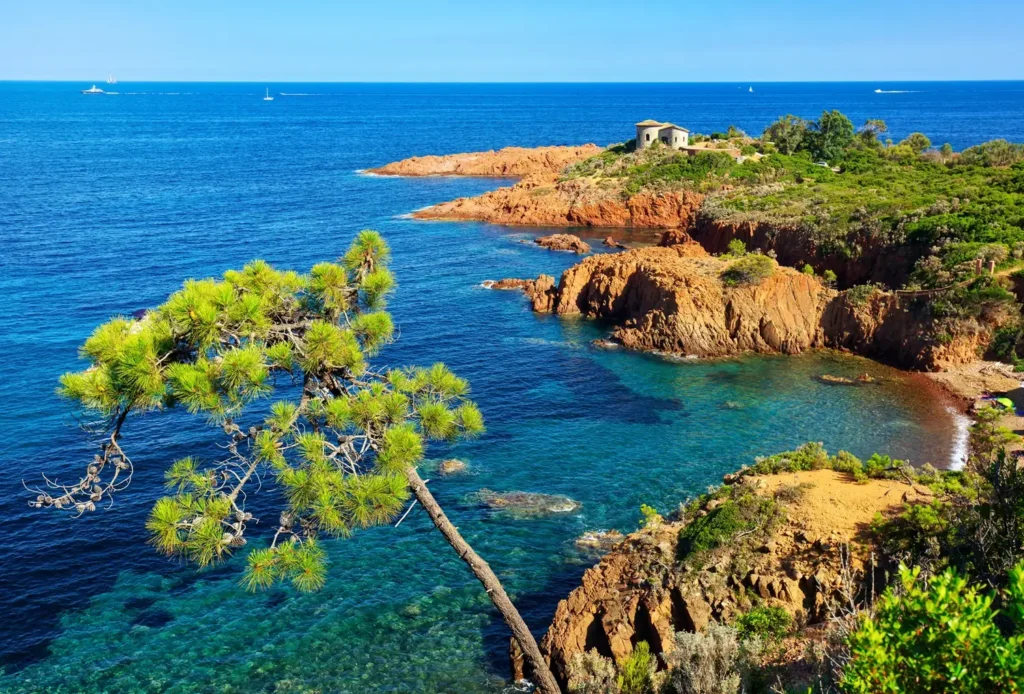 Aerial view of the rugged red volcanic rocks of the Massif de l'Esterel meeting the clear blue Mediterranean Sea.