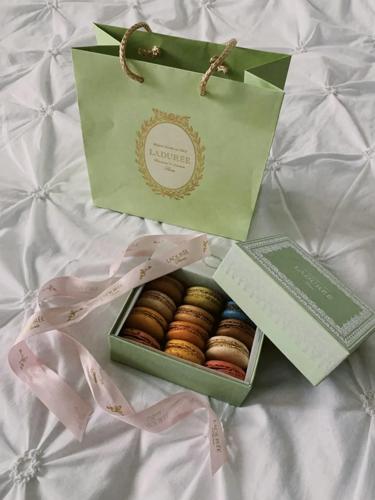 Ladurée signature green shopping bag and a box of assorted macarons on a white bedspread