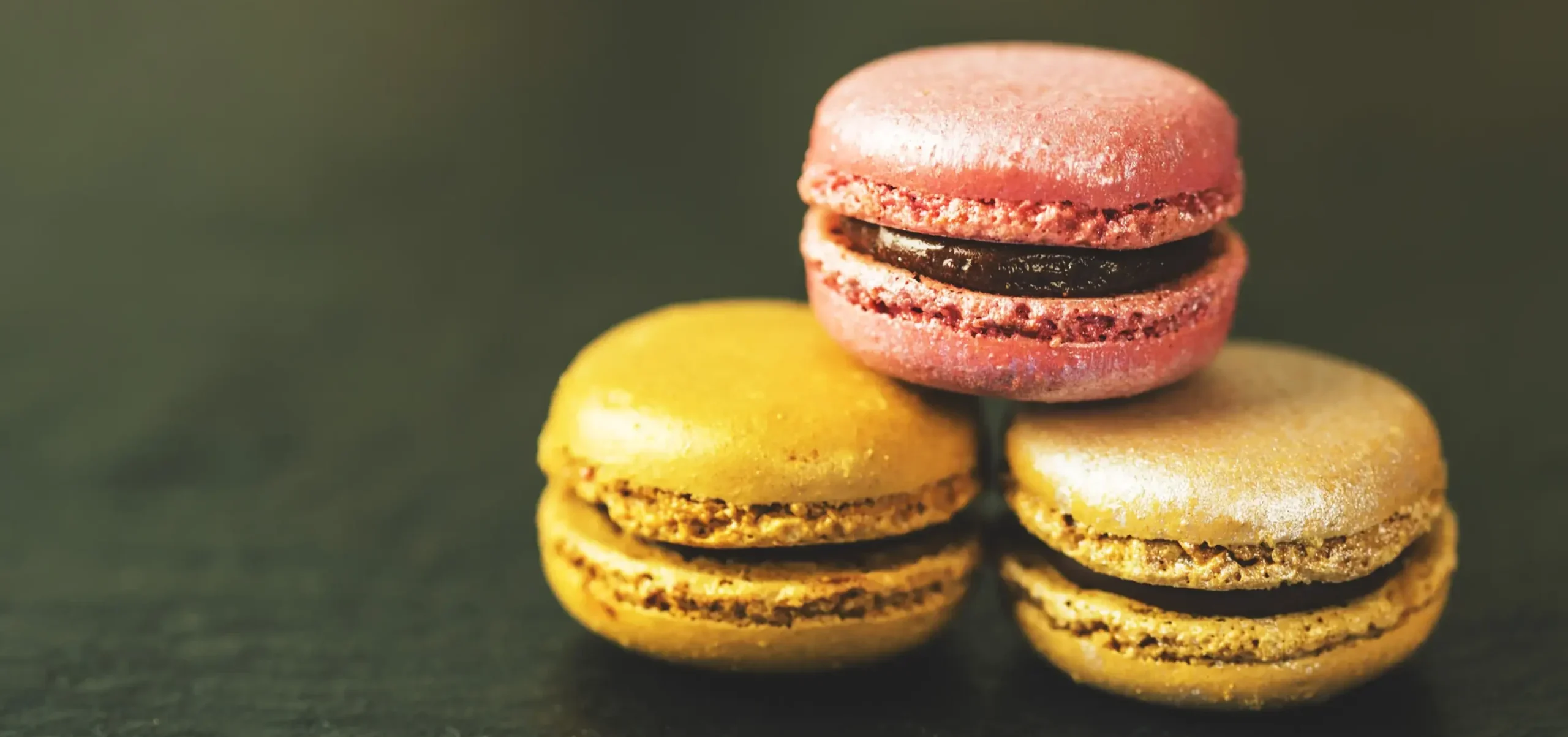 The Best Macarons in Paris - A stack of three colorful French macarons in pink, yellow, and gold flavors